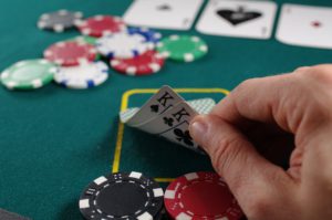 Representative image of a poker table with poker chips and a man's hand showing a pair of Kings