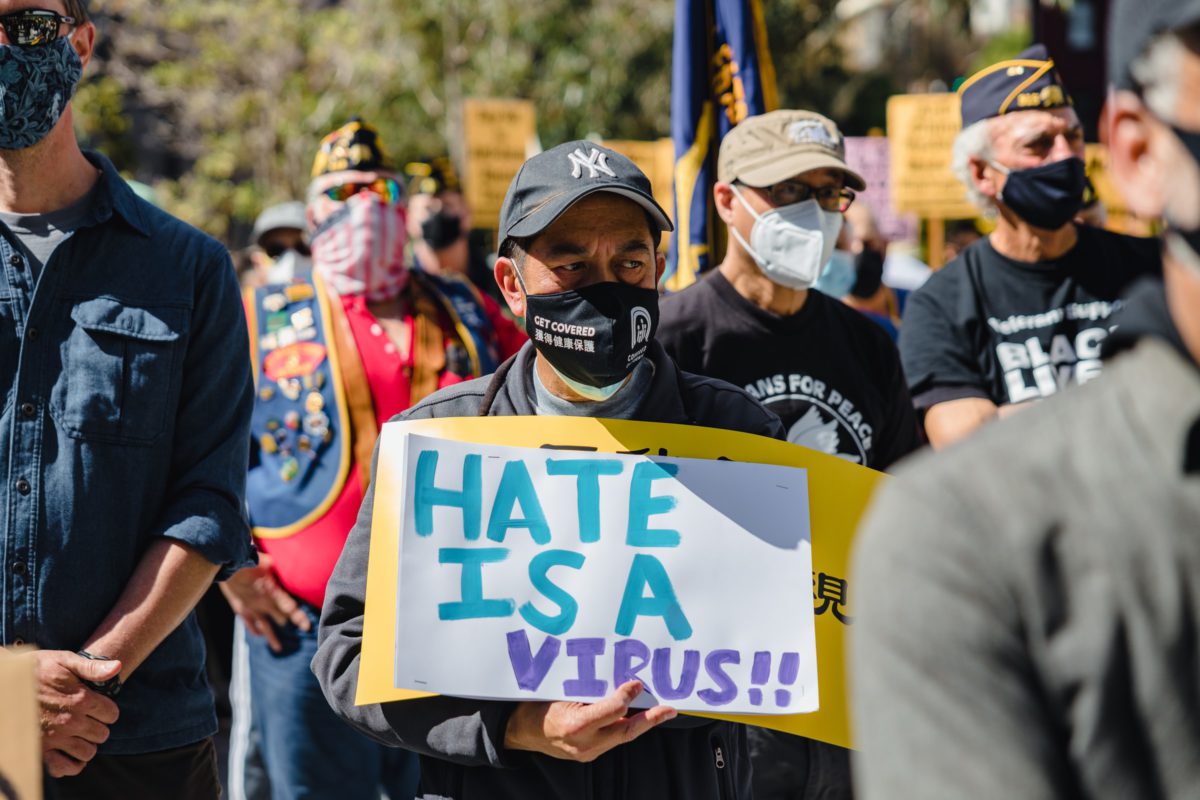 Representative photo of a man wearing a mask saying "Hate is a virus" | Photo by Jason Leung on Unsplash