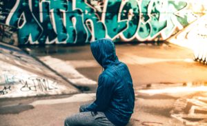 Representative image of a person wearing a sweatshirt sitting in front of a graffiti wall