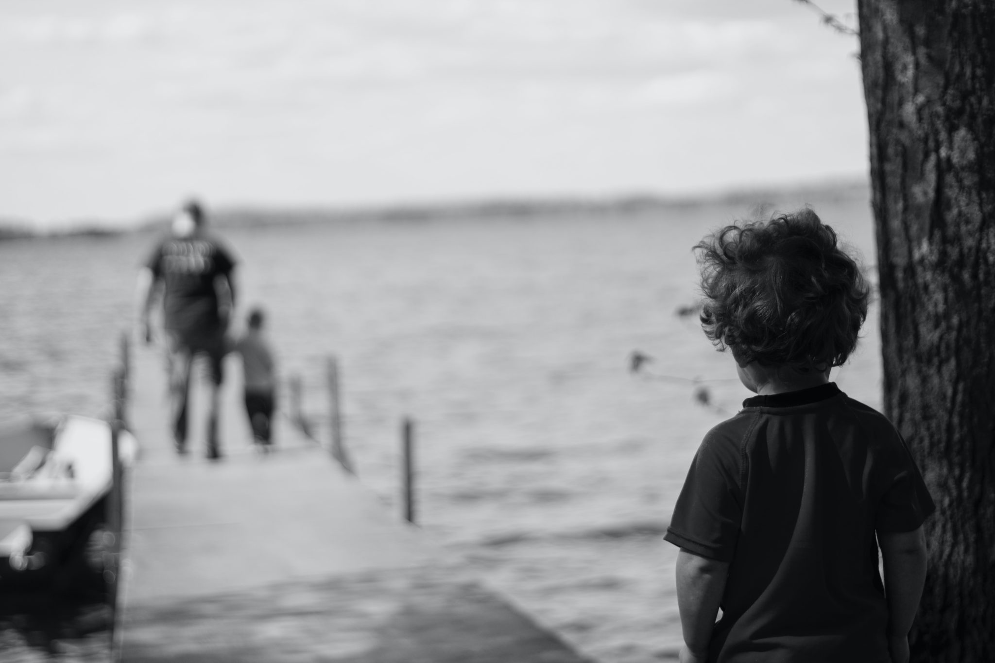 Grayscale image of a boy from a distance watching a man another boy walking on a pier.