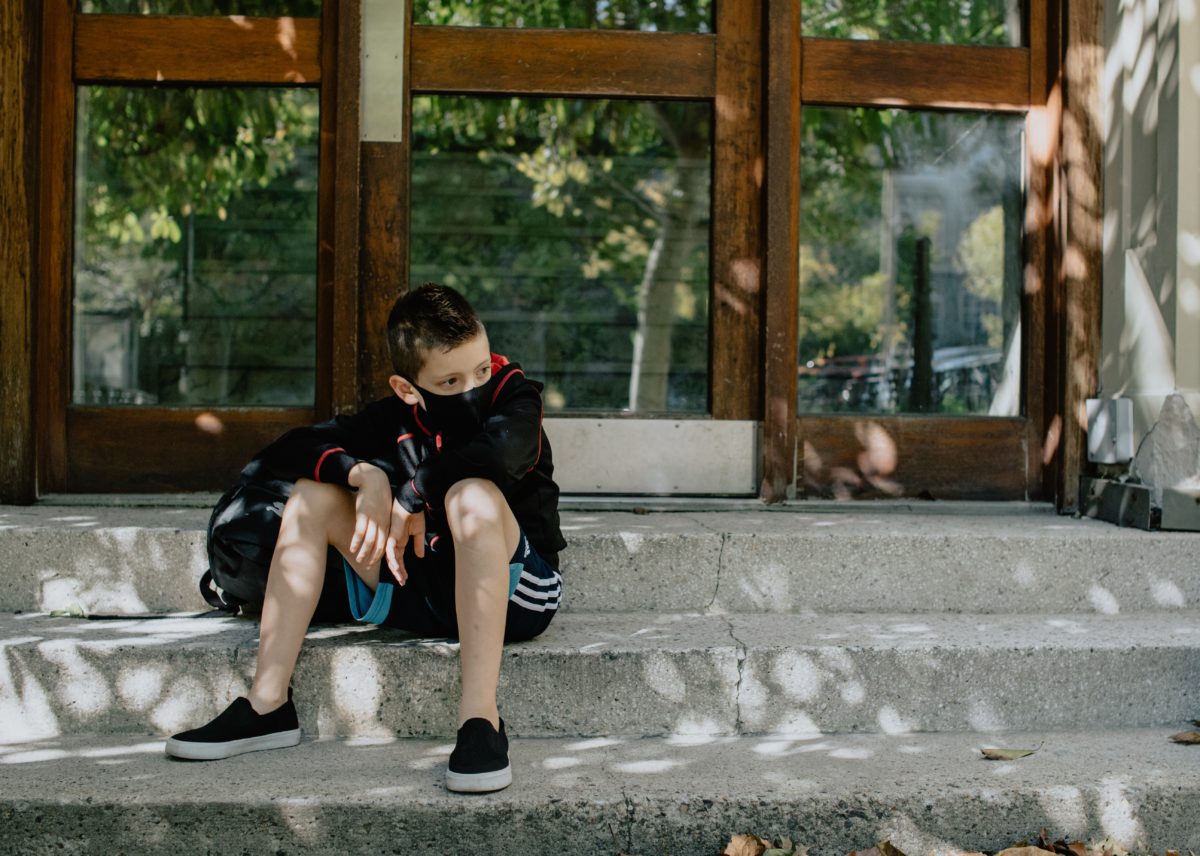 Photo of a young boy in a face mask sitting on steps