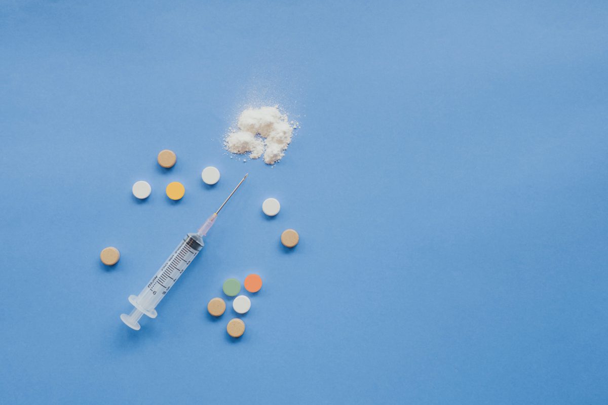 An overhead shot of a syringe, a white powder, and some pills on a blue background